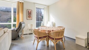 Uma sala de estar moderna com um sofá, uma mesa de jantar com cadeiras e uma janela grande com cortinas.