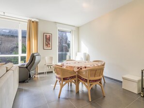 Ein modernes Wohnzimmer mit einer Couch, einem Esstisch mit Stühlen und einem großen Fenster mit Vorhängen.