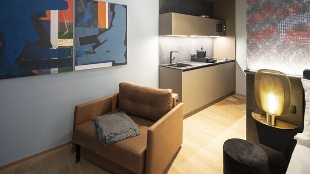 A modern living room with a sofa, a small table, and a wall-mounted lamp. - Backhome City Apartments (Innsbruck)