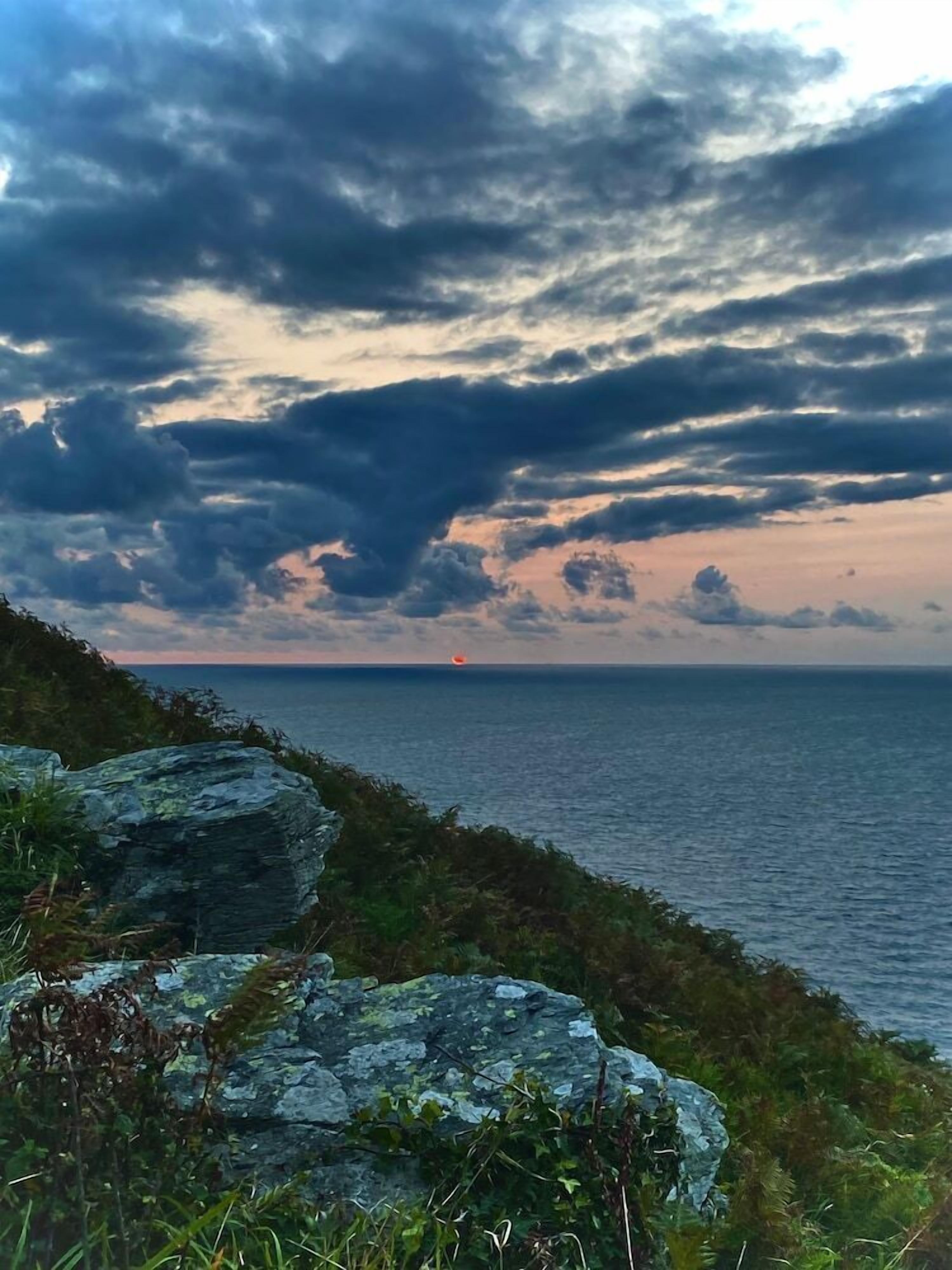 A coastal landscape with a rocky foreground and a view of the sea under a cloudy sky.