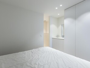Ein modernes Schlafzimmer mit einem großen Bett, einem Einbauschrank und einem durch eine offene Tür einsehbaren Badezimmer.