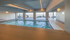Una piscina interior con vistas claras al océano y una zona de terraza de madera.