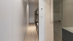 Un pasillo estrecho con suelo de madera, barandilla de metal negro y un termostato fijado a la pared.