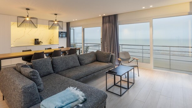 Una sala moderna con un amplio sofá seccional gris, una mesa de centro y un comedor con mesa y sillas de madera.
