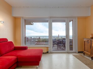 Una habitación con un sofá rojo, un armario de madera y un ventanal corredero que da a un balcón con vistas al mar.