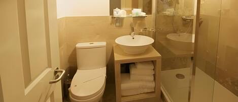 Un baño pequeño con inodoro, lavamanos y ducha con mampara de vidrio.