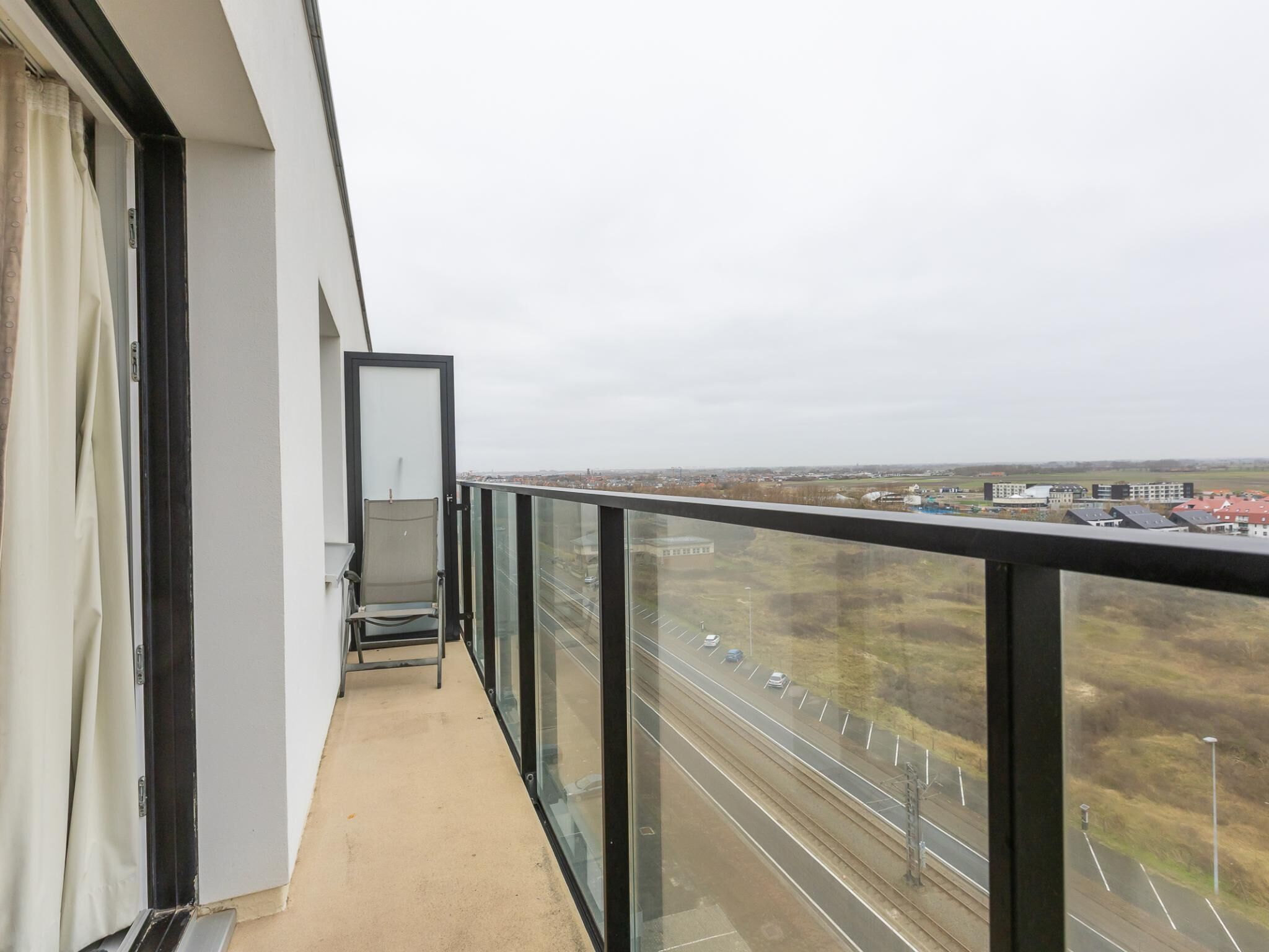 Un balcon doté d’une balustrade en verre, donnant sur une autoroute et des immeubles.
