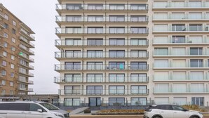 Un edificio residencial de varios pisos con balcones, una escalera y un estacionamiento con automóviles.