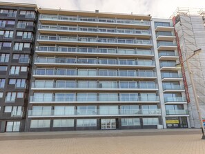 Un hôtel à plusieurs étages au design moderne, doté de balcons à chaque niveau et d’un hall d’entrée pavé de briques.