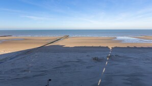 Ein Strand mit blauem Himmel, sandigem Ufer und einem hölzernen Steg, der sich ins Wasser erstreckt.