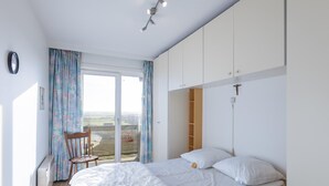 Ein Schlafzimmer mit einem großen Bett, einem Sessel, einem Schreibtisch und Blick auf die Landschaft durch eine Glastür.