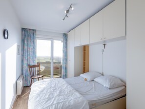 A bedroom with a large bed, a chair, a desk, and a view of the countryside through a sliding glass door. - Spacious apartment with garage and sea view (Middelkerke)