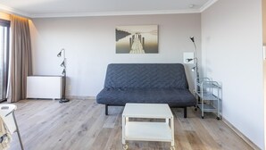 Ett modernt vardagsrum med en grå soffa, ett vitt soffbord, en tavla som föreställer en brygga och en vagn i metall.