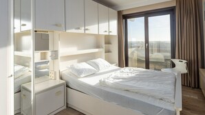 Ett modernt hotellrum med en stor säng, en garderob, ett nattduksbord och utsikt över staden genom ett stort fönster.