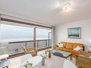 En moderne stue med stor balkon med udsigt over havet, møbleret med sofa, stole og sofabord.