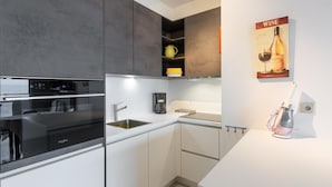 A modern kitchen with a built-in oven, a coffee maker, and a wine bottle on the wall. - Apartment with sea view and sunny terrace (Middelkerke)
