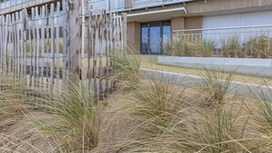 Un edificio de varios pisos con balcones, una valla de madera y hierba seca al frente.