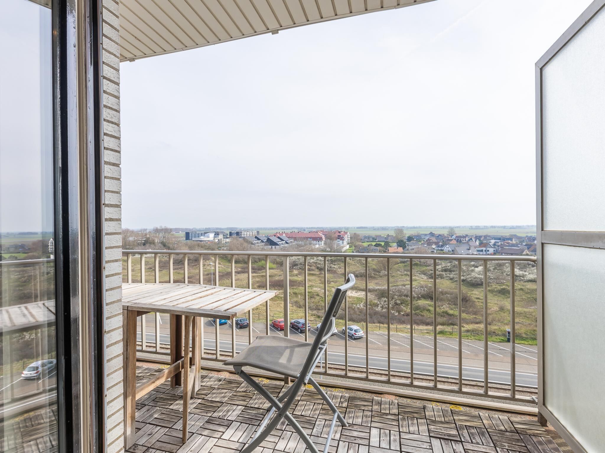 A balcony with a table and chair, overlooking a parking lot and buildings.