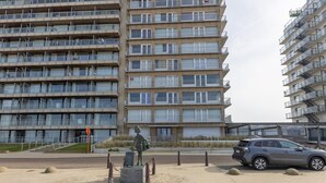 Un edificio residencial de varios pisos con balcones y una estatua de una persona con maleta en primer plano.