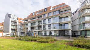 Un immeuble résidentiel moderne à plusieurs étages, doté de balcons, de grandes fenêtres et d’un toit plat.