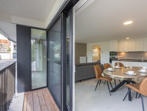 Un appartement moderne doté d’un balcon, d’un coin repas avec une table ronde et des chaises, et d’une cuisine avec des meubles blancs.