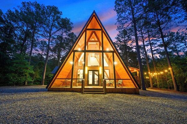 Une cabane triangulaire en bois, dotée d’une façade en verre et entourée d’arbres.