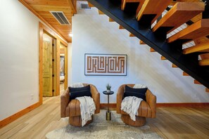 A modern interior with a wooden staircase, two leather armchairs, a small table with a plant, and a wall-mounted artwork.