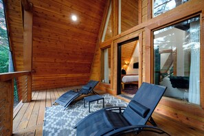 A wooden cabin with a balcony, two lounge chairs, and a bed with a view.