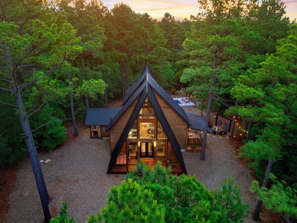 A cabin with a triangular roof, surrounded by dense forest.