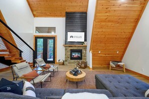 A modern living room with a fireplace, wooden ceiling, and a staircase leading to an upper level.