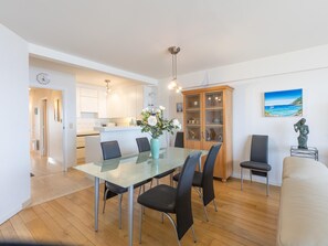 A modern kitchen with white cabinets, a central island, and a dining area with a glass table and black chairs. - Apartment with 2 bedrooms and sea view (Middelkerke)