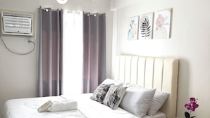 Un letto rifatto con un comofort bianco e cuscini, un comodino con un vaso di fiori e un lampadario.