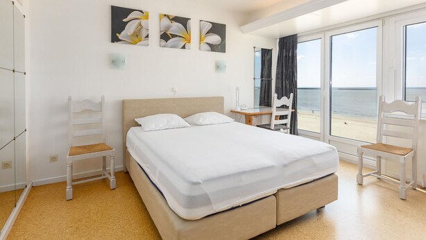 Une chambre d’hôtel avec un lit, un bureau, une chaise et une vue sur la plage.