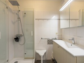 A modern bathroom with a glass-enclosed shower, a white sink, and a mirror above the sink. - Apartment with sea view and shared pool (Middelkerke)