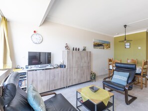Un salon comprenant un canapé, une table basse, un téléviseur, un meuble en bois et un coin repas avec des chaises et une table.