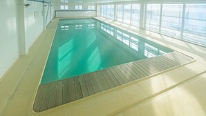 Une piscine intérieure à l’eau claire, dotée de grandes fenêtres et d’un sol carrelé.