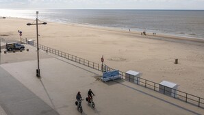 Une plage avec une promenade dallée, des bancs et une poubelle.