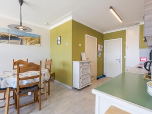 A compact kitchen with a dining area, featuring a table with chairs, a refrigerator, and a small island. - Apartment with sea view and shared pool (Middelkerke)