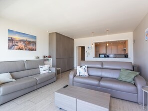 A modern living room with two sofas, a coffee table, and a kitchen in the background. - Spacious apartment on the seafront (Middelkerke)