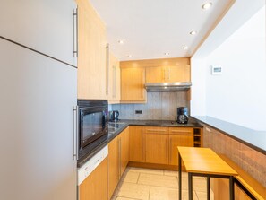 A modern kitchen with wooden cabinets, a stainless steel oven, a coffee maker, and a small table. - Spacious apartment on the seafront (Middelkerke)
