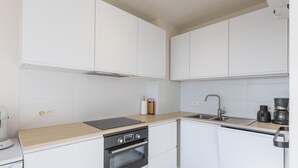Une cuisine moderne avec des meubles blancs, un four noir, un évier et une machine à café.