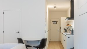 Una stanza funzionale con un letto, un tavolo da pranzo con due sedie, angolo cottura e una porta.