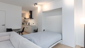Una camera da letto moderna e funzionale, con un letto singolo, una scrivania e angolo cottura sullo sfondo.