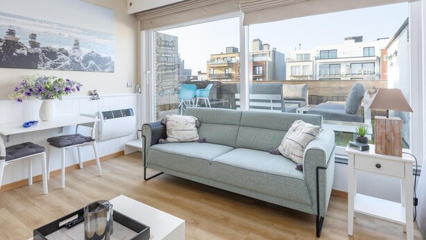 A modern living room with a grey sofa, white furniture, and a city view through large windows. - Studio with sunny rooftop terrace near the sea (Middelkerke)