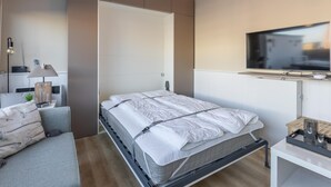 A modern bedroom with a bed, bedside table, lamp, and a TV mounted on the wall. - Studio with sunny rooftop terrace near the sea (Middelkerke)