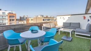A rooftop terrace with a round table and blue chairs, a grey sofa, and a white wall with decorative elements. - Studio with sunny rooftop terrace near the sea (Middelkerke)