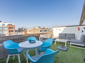 A rooftop terrace with a round table and blue chairs, a grey sofa, and a white wall with decorative elements. - Studio with sunny rooftop terrace near the sea (Middelkerke)
