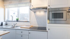 A modern kitchen with white cabinetry, a stainless steel range hood, a built-in microwave, and a window with a view of the outside. - Studio with sunny rooftop terrace near the sea (Middelkerke)