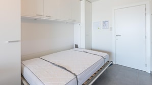 A bedroom with a bed, built-in wardrobe, and a door with a control panel. - Charming studio on the seafront with sea view (Middelkerke)