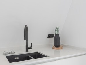 A modern kitchen with a black faucet, a sink, and a potted plant on a white countertop. - Spacious apartment with 3bedrooms close to  sea (Middelkerke)